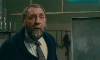 Movie still from “7 Rm., kit., ba...” (1984), directed by Agnès Varda – An older man with a gray beard wearing a tie; Close Up shot, Over the shoulder angle