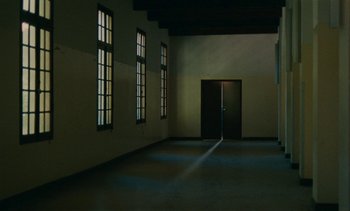 Movie still from “7 Rm., kit., ba...” (1984), directed by Agnès Varda – An empty room with two windows and a black door; Extreme Wide shot, High angle