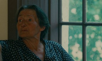 Movie still from “7 Rm., kit., ba...” (1984), directed by Agnès Varda – An older woman sitting in front of a window; Close Up shot, Low angle