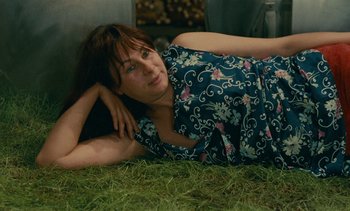 Movie still from “7 Rm., kit., ba...” (1984), directed by Agnès Varda – A woman laying in the grass looking at the camera; Medium shot, High angle