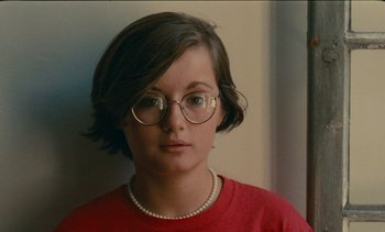 Movie still from “7 Rm., kit., ba...” (1984), directed by Agnès Varda – A woman wearing glasses and a red shirt; Close Up shot, High angle