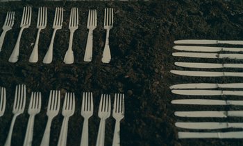 Movie still from “7 Rm., kit., ba...” (1984), directed by Agnès Varda – A bunch of silverware sitting on top of a dirt ground; Extreme Close Up shot, Overhead angle