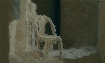 Movie still from “7 Rm., kit., ba...” (1984), directed by Agnès Varda – A chair covered in snow in front of a wall; Wide shot, High angle