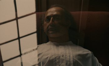 Movie still from “7 Rm., kit., ba...” (1984), directed by Agnès Varda – A man in a white dress shirt is looking out of a window; Close Up shot, Low angle