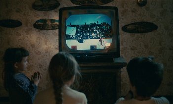 Movie still from “7 Rm., kit., ba...” (1984), directed by Agnès Varda – Two young children watching television in a living room; Medium shot, Over the shoulder angle