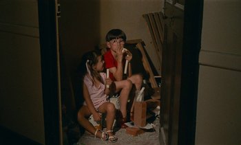Movie still from “7 Rm., kit., ba...” (1984), directed by Agnès Varda – Two children sitting on a toilet in a room; Medium shot, High angle