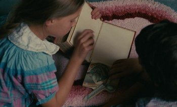 Movie still from “7 Rm., kit., ba...” (1984), directed by Agnès Varda – A young girl is reading a book while another looks on; Close Up shot, High angle