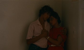 Movie still from “7 Rm., kit., ba...” (1984), directed by Agnès Varda – Two people are hugging in a corner of a room; Medium shot, High angle