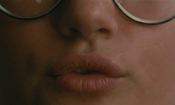 Movie still from “7 Rm., kit., ba...” (1984), directed by Agnès Varda – View of a woman's lips and glasses; Extreme Close Up shot, Over the shoulder angle