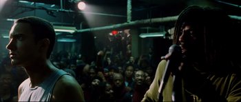 Movie still from “8 Mile” (2002), directed by Curtis Hanson – A group of people sitting in front of a microphone in a room; Medium shot, Over the shoulder angle
