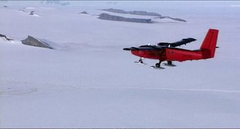 Movie still from “9 Songs” (2004), directed by Michael Winterbottom – A red plane flying over a snow covered field; Extreme Wide shot, High angle