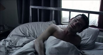 Movie still from “9 Songs” (2004), directed by Michael Winterbottom – A man laying in a bed with his eyes closed; Medium shot, High angle