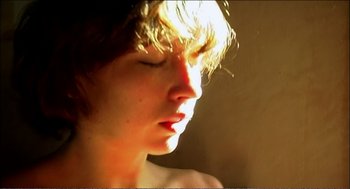 Movie still from “9 Songs” (2004), directed by Michael Winterbottom – A young man with short brown hair is looking into the light; Extreme Close Up shot, High angle
