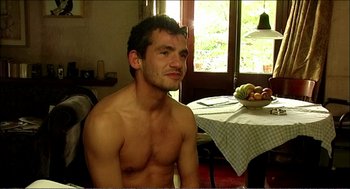 Movie still from “9 Songs” (2004), directed by Michael Winterbottom – A man sitting in front of a bowl of fruit; Medium shot, High angle