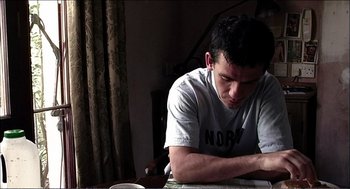 Movie still from “9 Songs” (2004), directed by Michael Winterbottom – A man sitting at a table with a cup in front of him; Medium shot, Low angle