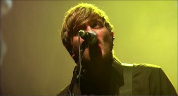 Movie still from “9 Songs” (2004), directed by Michael Winterbottom – A man with a microphone in his mouth; Close Up shot, Low angle