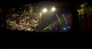 Movie still from “9 Songs” (2004), directed by Michael Winterbottom – A crowd of people on a stage at a concert; Extreme Wide shot, High angle