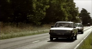 Movie still from “9 Songs” (2004), directed by Michael Winterbottom – A car driving down a road near some trees; Wide shot, Low angle