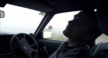 Movie still from “9 Songs” (2004), directed by Michael Winterbottom – A man sitting in the driver's seat of a car; Close Up shot, High angle
