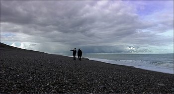 Movie still from “9 Songs” (2004), directed by Michael Winterbottom – Two people standing on a beach looking out at the ocean; Extreme Wide shot, Low angle