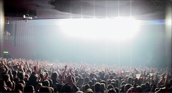 Movie still from “9 Songs” (2004), directed by Michael Winterbottom – A large crowd of people in a large stadium; Extreme Wide shot, Low angle