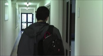Movie still from “9 Songs” (2004), directed by Michael Winterbottom – A person with a backpack walking down a hallway; Wide shot, Over the shoulder angle