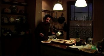 Movie still from “9 Songs” (2004), directed by Michael Winterbottom – A man standing in front of a table with food; Wide shot, High angle
