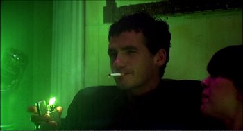Movie still from “9 Songs” (2004), directed by Michael Winterbottom – A man sitting in a chair with a cigarette in his mouth; Close Up shot, Low angle
