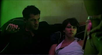 Movie still from “9 Songs” (2004), directed by Michael Winterbottom – A man and a woman sitting next to each other on a couch; Medium shot, High angle
