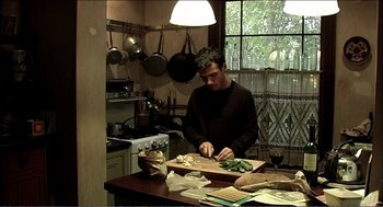 Movie still from “9 Songs” (2004), directed by Michael Winterbottom – A man cutting vegetables in a kitchen with pots on the wall; Medium shot, High angle