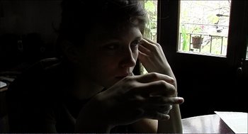 Movie still from “9 Songs” (2004), directed by Michael Winterbottom – A woman sitting in front of a window holding her hand to her face; Close Up shot, High angle