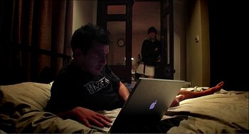 Movie still from “9 Songs” (2004), directed by Michael Winterbottom – A man and a woman on a bed using a laptop; Wide shot, High angle