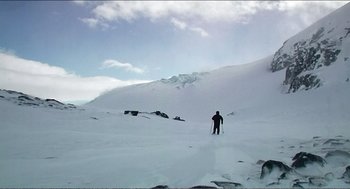 Movie still from “9 Songs” (2004), directed by Michael Winterbottom – A person on skis is standing in the middle of a snow covered slope; Extreme Wide shot, High angle
