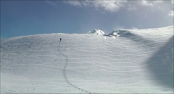 Movie still from “9 Songs” (2004), directed by Michael Winterbottom – A person is skiing down a snowy slope; Extreme Wide shot, High angle