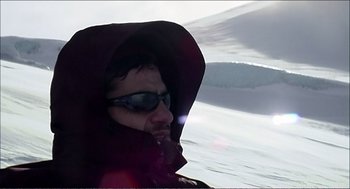 Movie still from “9 Songs” (2004), directed by Michael Winterbottom – A man wearing a hood and sunglasses on a boat in the water; Close Up shot, High angle