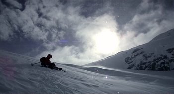 Movie still from “9 Songs” (2004), directed by Michael Winterbottom – A person sitting in the snow on a mountain; Extreme Wide shot, Low angle