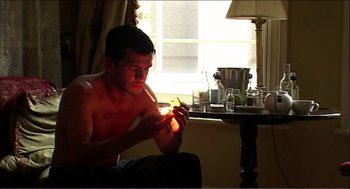 Movie still from “9 Songs” (2004), directed by Michael Winterbottom – A man sitting on the floor holding a lit candle; Medium shot, Low angle