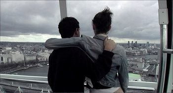Movie still from “9 Songs” (2004), directed by Michael Winterbottom – A man and a woman are looking at a city; Medium shot, Low angle