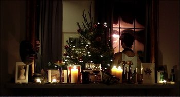 Movie still from “9 Songs” (2004), directed by Michael Winterbottom – A woman sitting in front of a small christmas tree; Medium shot, Over the shoulder angle