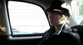 Movie still from “9 Songs” (2004), directed by Michael Winterbottom – A woman sitting in the back seat of a car; Close Up shot, Over the shoulder angle