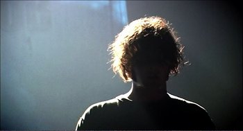 Movie still from “9 Songs” (2004), directed by Michael Winterbottom – A man with a messy hair style in the dark; Close Up shot, Low angle