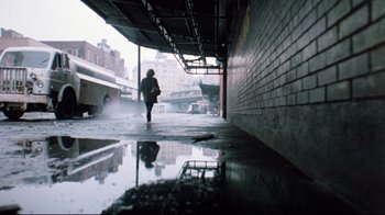 Movie still from “9½ Weeks” (1986), directed by Adrian Lyne – A person is walking down the street in the rain; Wide shot, Low angle