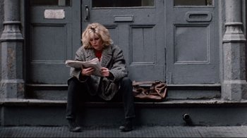 Movie still from “9½ Weeks” (1986), directed by Adrian Lyne – A woman sitting on the steps reading a newspaper; Wide shot, Low angle