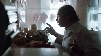 Movie still from “9½ Weeks” (1986), directed by Adrian Lyne – A man sitting in front of a bunch of food on a table; Close Up shot, Over the shoulder angle
