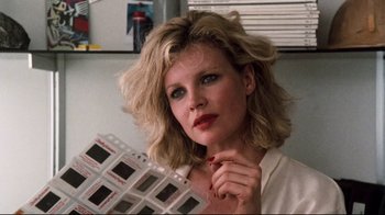 Movie still from “9½ Weeks” (1986), directed by Adrian Lyne – A woman with blonde hair holding a strip of negatives in her hand; Close Up shot, Low angle