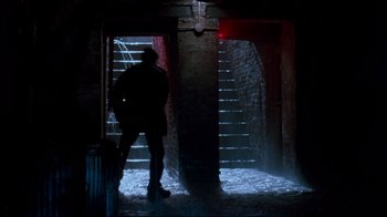 Movie still from “9½ Weeks” (1986), directed by Adrian Lyne – A man standing in a dark room next to stairs; Wide shot, Low angle