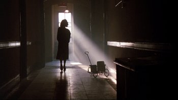 Movie still from “9½ Weeks” (1986), directed by Adrian Lyne – A woman standing in a room with a cart in front of a door; Wide shot, Low angle