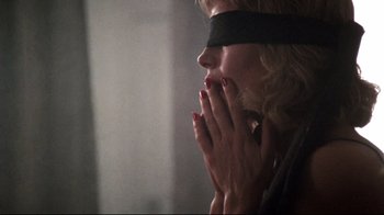 Movie still from “9½ Weeks” (1986), directed by Adrian Lyne – A blindfolded woman with her hands over her mouth; Close Up shot, Over the shoulder angle