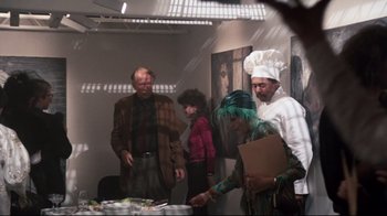 Movie still from “9½ Weeks” (1986), directed by Adrian Lyne – A group of people standing around a table with food on top of it; Medium shot, High angle