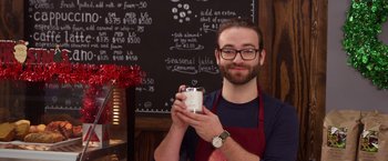 Movie still from “A Bad Moms Christmas” (2017), directed by Scott Moore – A man holding a cup of coffee in front of a chalkboard; Close Up shot, High angle